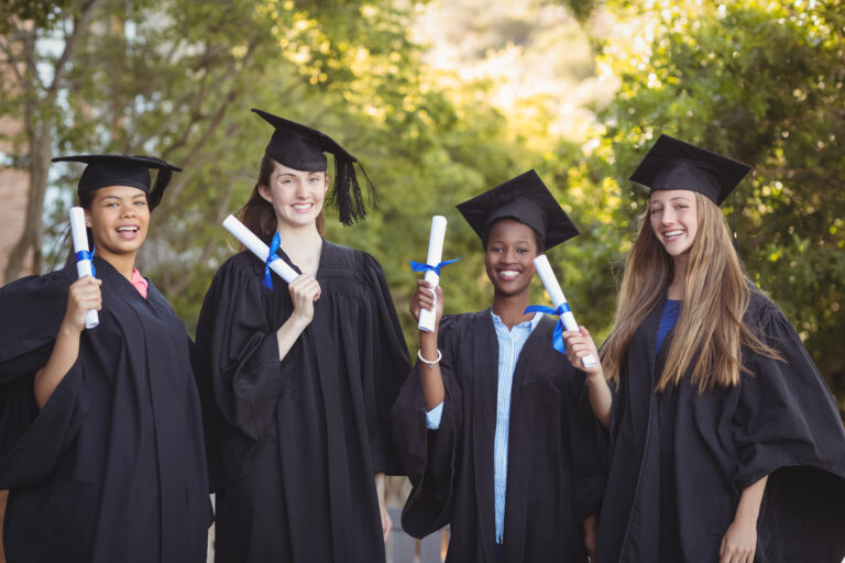 Four graduates celebrating on campus with their degree scrolls